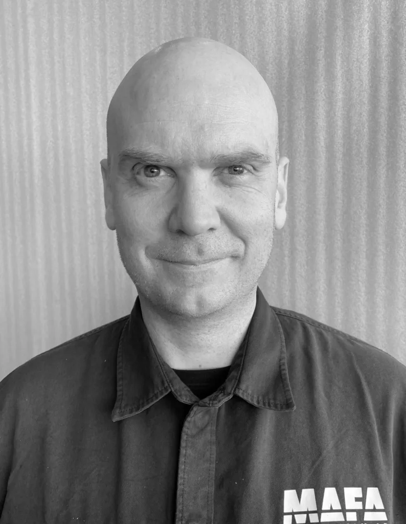 Daniel Törnblad framför en industriell väggkonstruktion, med MAEA-logotypen synlig på skjortan.
